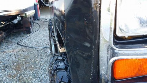 1984 Ford Bronco - Side view of a black Ford Bronco's front fender and headlight assembly. Off-road tire is mounted.