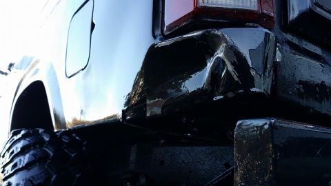 1984 Ford Bronco - The rear corner of a black SUV shows a dented bumper and a large tire.