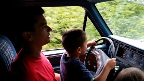 1984 Ford Bronco - A boy pretends to drive while a man watches from the passenger seat inside a vehicle.