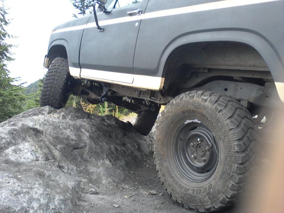 Modified Ford Bronco with large tires climbing over rocks