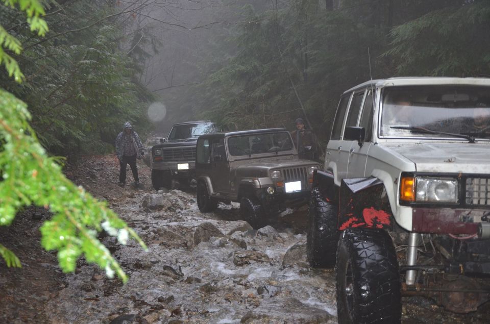 White SUV and brown Jeep on a muddy, rocky forest road with trees