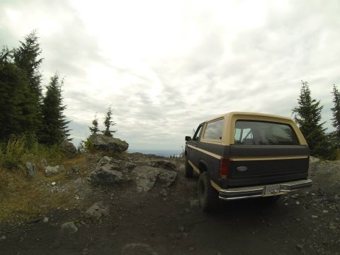1984 Ford Bronco - 1984 Ford Bronco parked on a rocky mountain overlook with a cloudy sky.