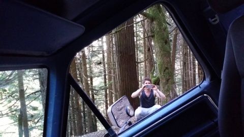 1984 Ford Bronco - A person is photographed from inside a vehicle while squatting in a wooded area.