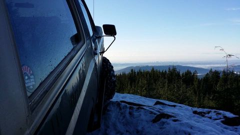 1984 Ford Bronco - SUV parked on snowy mountain overlooking a distant city skyline.