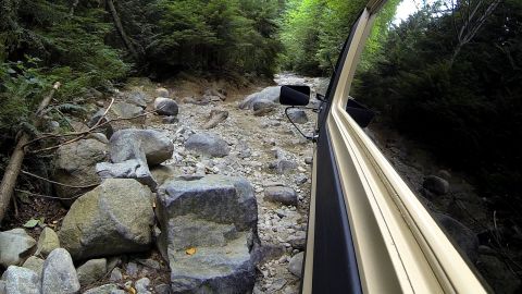 1984 Ford Bronco - Navigating a challenging, boulder-strewn path through a dense forest.