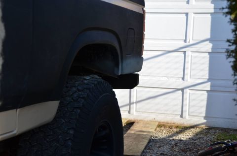 1984 Ford Bronco - The rear section of an SUV is visible, with a large tire and a portion of the bodywork against a garage door.