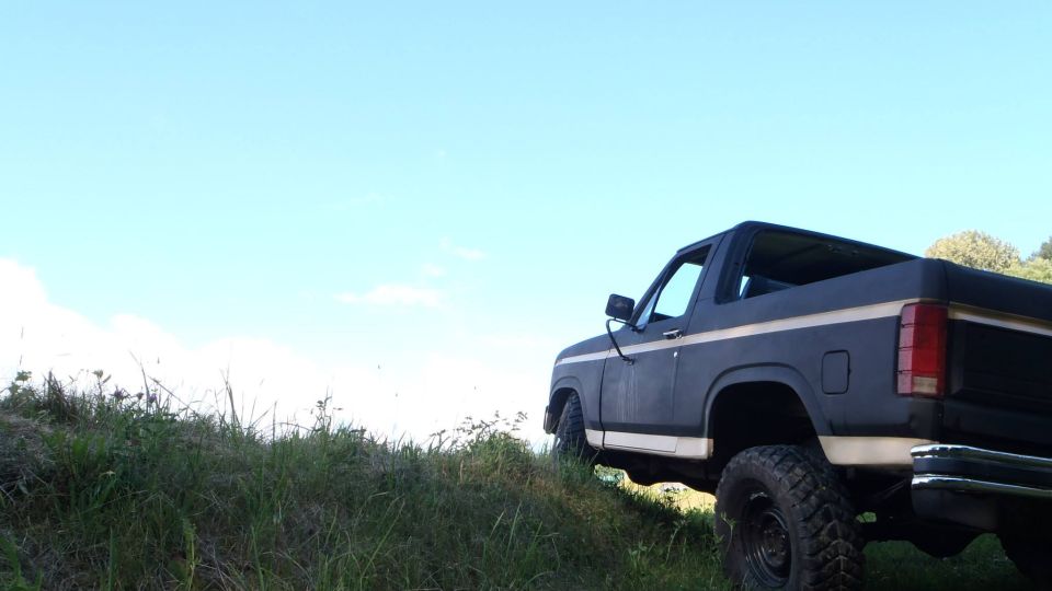 Dark blue SUV with white stripe, seen from rear quarter, on grassy hill under blue sky
