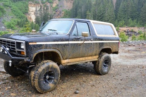1984 Ford Bronco - This 1984 Ford Bronco, seen here in a 3/4 front view, is heavily covered in mud, suggesting off-road use.