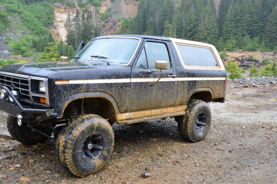 Mud-covered black 1984 Ford Bronco with tan top, 3/4 front view