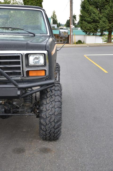 1984 Ford Bronco - This modified Ford Bronco features aggressive off-road tires and a custom front bumper, suggesting it's built for terrain.