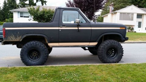 1984 Ford Bronco - Modified black Ford Bronco with large off-road tires and a tan stripe accent.