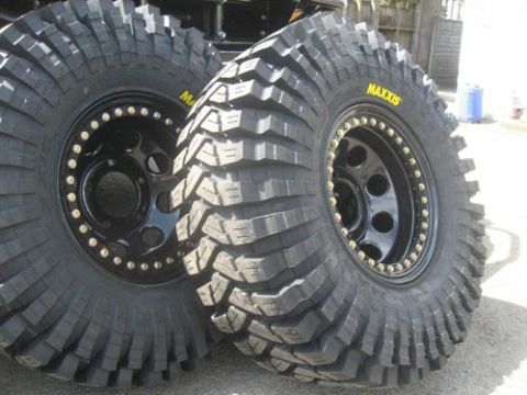 1984 Ford Bronco - Close-up of two aggressive off-road tires mounted on black rims with gold hardware.