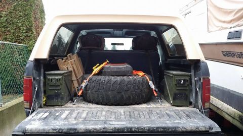 1984 Ford Bronco - Rear view of a tan and black Ford Bronco loaded with gear, including a spare tire and ammo cans.