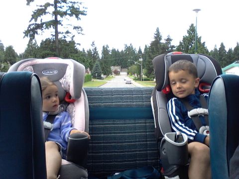 1984 Ford Bronco - Two children are secured in car seats in the back of a vehicle, with a view of a residential street ahead.