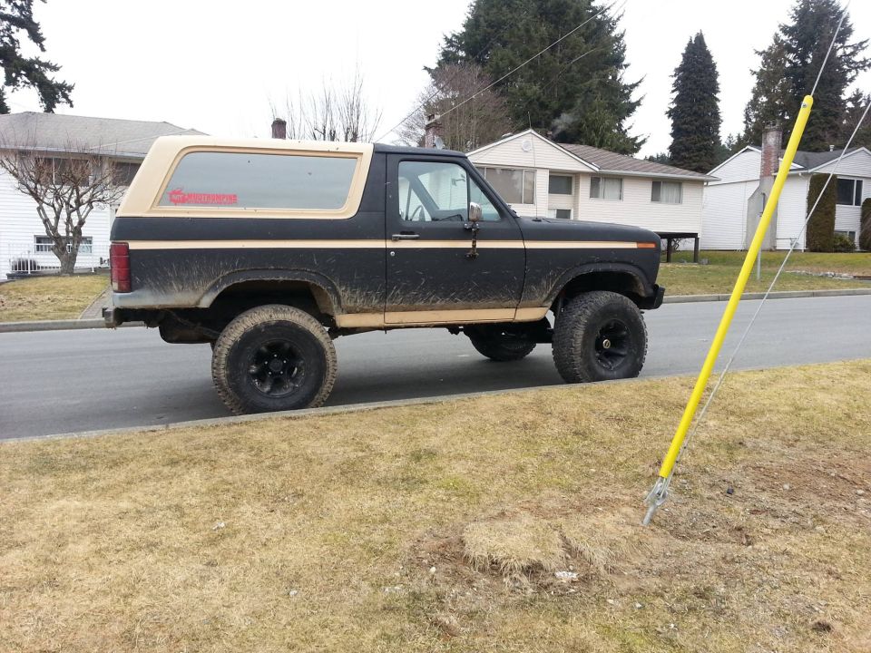 Black Ford Bronco with tan top parked on a residential street, lifted with off-road tires. Red sticker on rear window