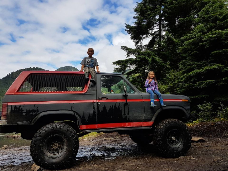 Black and red Ford Bronco with red trim, children on roof and hood