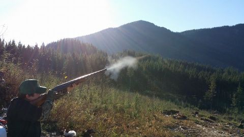 1984 Ford Bronco - A person fires a rifle, creating smoke, against a backdrop of forested mountains under a bright sky.