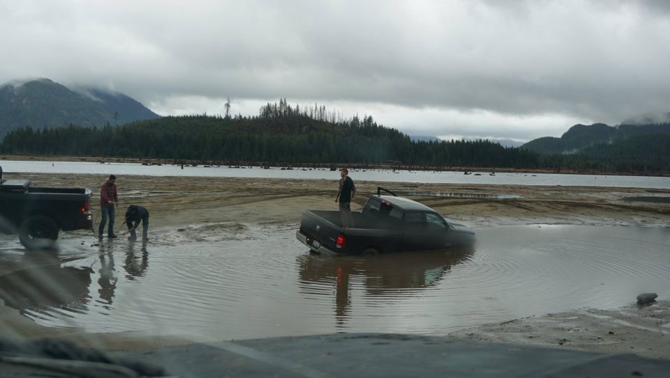 Black pickup truck partially submerged in muddy water with two people nearby
