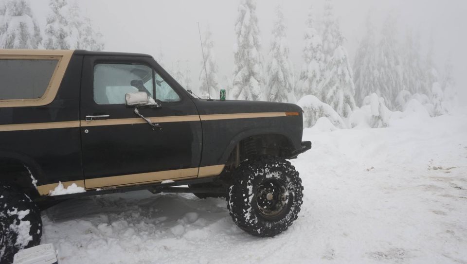 Black and tan Ford Bronco with large tires in the snow