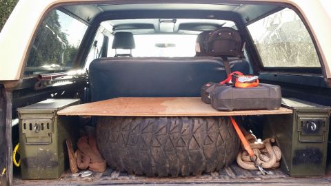 1984 Ford Bronco - The cargo area of an SUV is organized with a spare tire, ammo cans, and recovery gear.