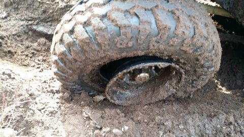 1984 Ford Bronco - A vehicle's tire is stuck in the mud, with the rim visibly bent.