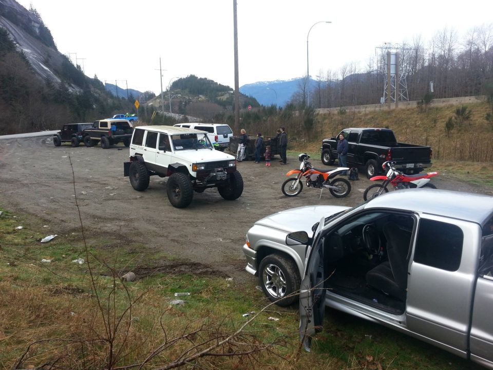 White off-road SUV with large tires parked in a dirt lot with other vehicles and motorcycles