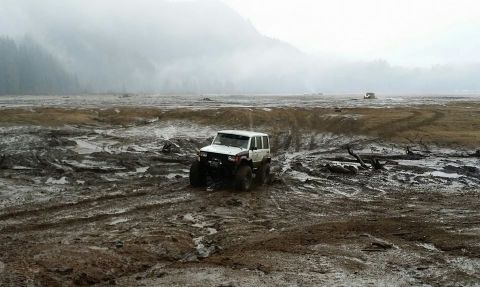 1984 Ford Bronco - A modified off-road vehicle navigates a challenging muddy terrain under overcast skies.