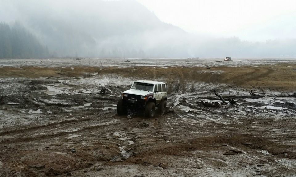 Off-road vehicle driving through a muddy field with hills in the background