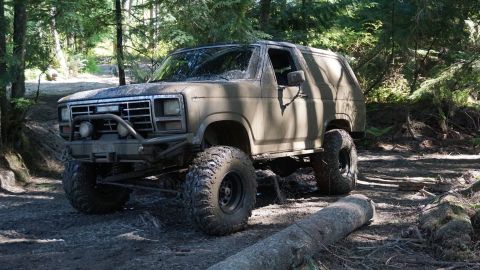 1984 Ford Bronco - This modified SUV navigates a wooded trail, its large tires and build suited for off-road adventures.