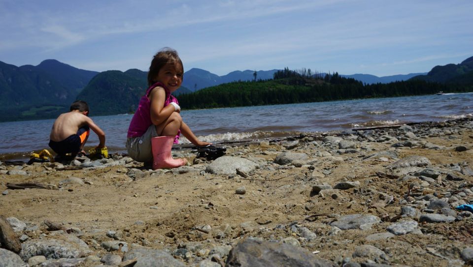 Two kids play on a beach by a lake with mountains in the background