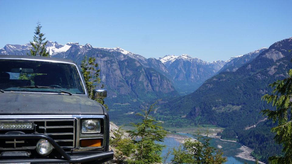Front view of a dark gray Ford Bronco parked on a mountain overlook, with a river valley and snow-capped mountains in the background
