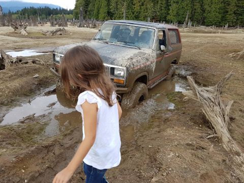 1984 Ford Bronco - A child walks past a mud-splattered Ford Bronco stuck in a muddy, desolate landscape.