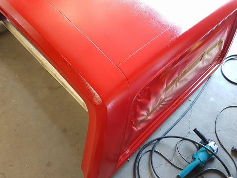 1984 Ford Bronco - Vehicle body panel being painted red, with masking tape applied to protect an opening.