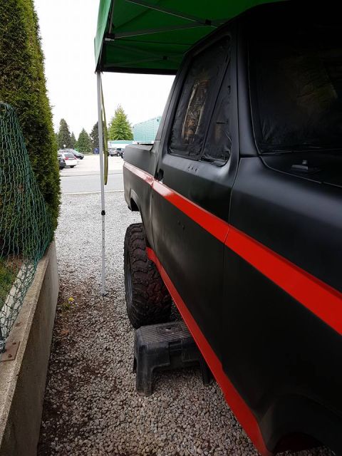 1984 Ford Bronco - A black pickup truck with a red stripe is parked outside under a green canopy, with large tires visible.