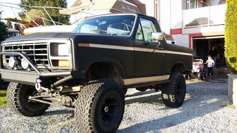 1984 Ford Bronco - Modified black SUV with a beige stripe and lifted suspension sits in a driveway.