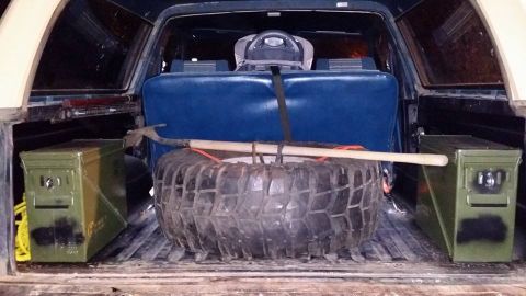 1984 Ford Bronco - Cargo area of an SUV loaded with a spare tire, shovel, and two ammo cans.
