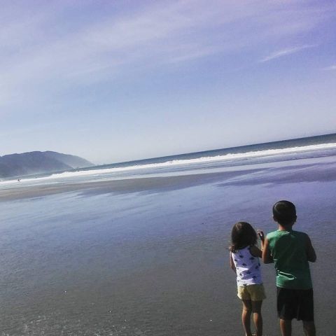 1984 Ford Bronco - Children observe the ocean waves on a wide, flat beach with distant mountains.