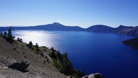 1984 Ford Bronco - A scenic view of Crater Lake, surrounded by mountains and dotted with trees on the shoreline.