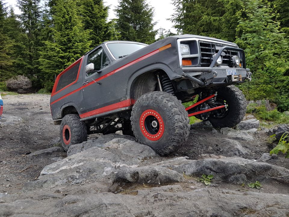 Modified Ford Bronco with large tires and red beadlock wheels on rocky terrain