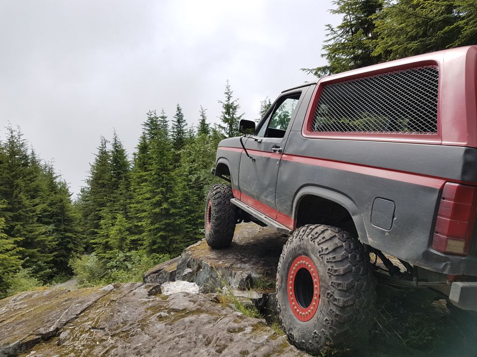 1984 Ford Bronco with red trim and large tires on a rocky cliffside