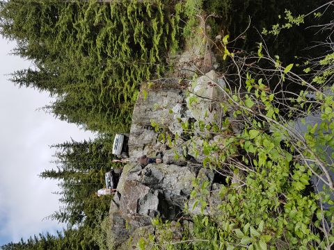 1984 Ford Bronco - Two white SUVs are parked precariously on a rocky cliff face, surrounded by trees.