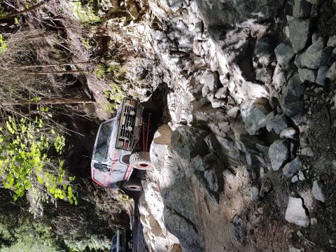 1984 Ford Bronco - Off-road truck navigating a challenging rocky trail with trees and cliffs.