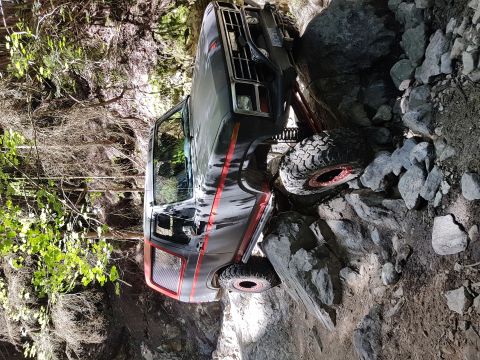 1984 Ford Bronco - This dark SUV with red trim is navigating a challenging rocky trail, appearing to be from the early 1980s.