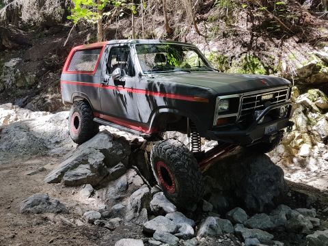1984 Ford Bronco - This modified Ford Bronco navigates a rocky trail, demonstrating its off-road capabilities.