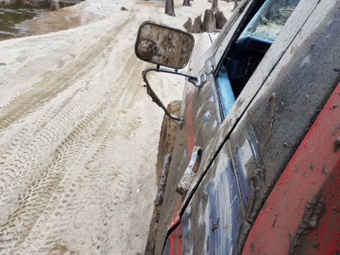 1984 Ford Bronco - A heavily soiled vehicle is viewed from the side, with tire tracks visible in the sand.