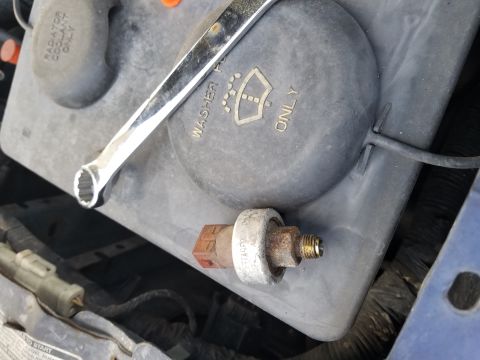 1994 Ford Bronco - A wrench rests on a washer fluid reservoir next to a removed sensor in a vehicle's engine bay.