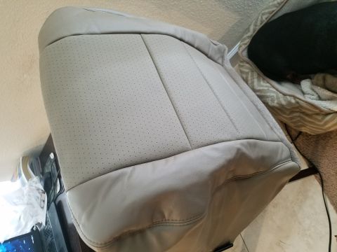 1994 Ford Bronco - Close-up of a light gray perforated leather car seat, showing stitching and texture. A dog rests in a bed in the background.