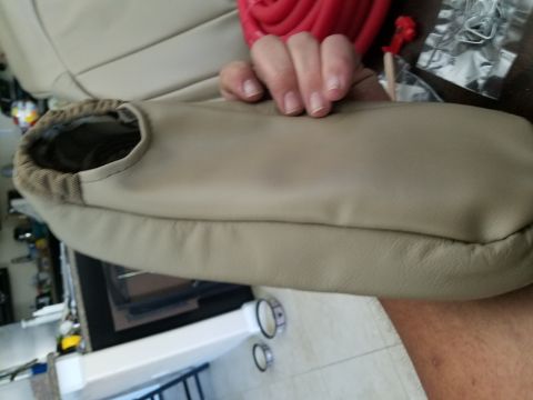 1994 Ford Bronco - A hand holds a tan car seat armrest cover with a patterned interior lining.