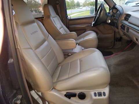 1994 Ford Bronco - The interior features tan leather captain's chairs with visible power seat controls.