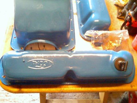 1989 Ford Bronco - Two blue Ford valve covers are visible on a wooden surface, with a plastic bag of parts in the background.